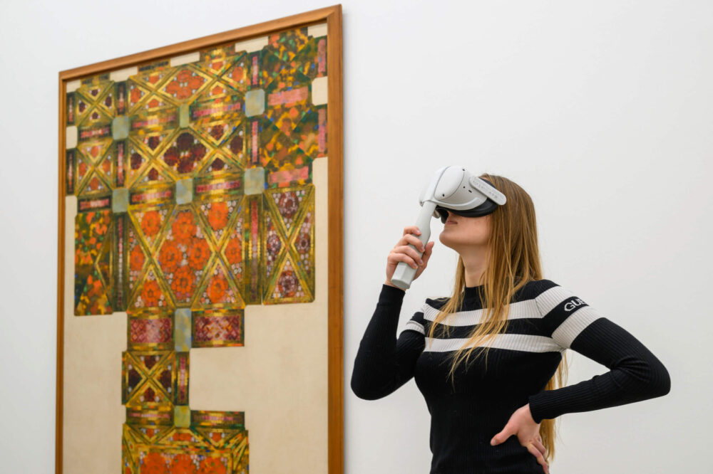 Eine Frau steht vor einem Werk von Augusto Giacometti und schaut in eine VR Brille