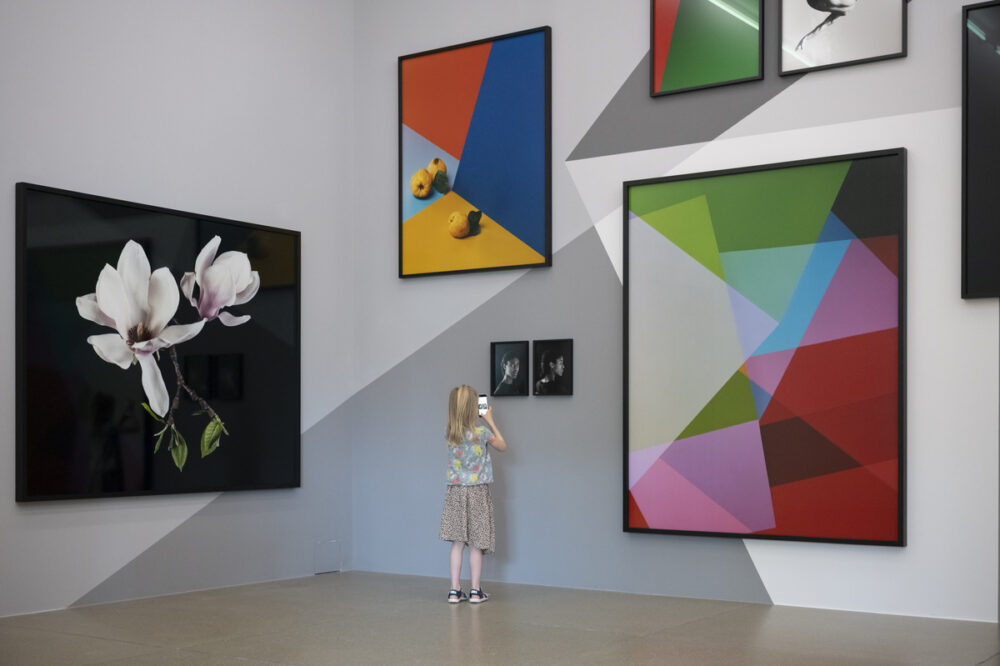 Ein Kind, das vor mehreren farbigen, abstrakten Fotografieren auf einer mit grauen Muster bemalten Wand steht
