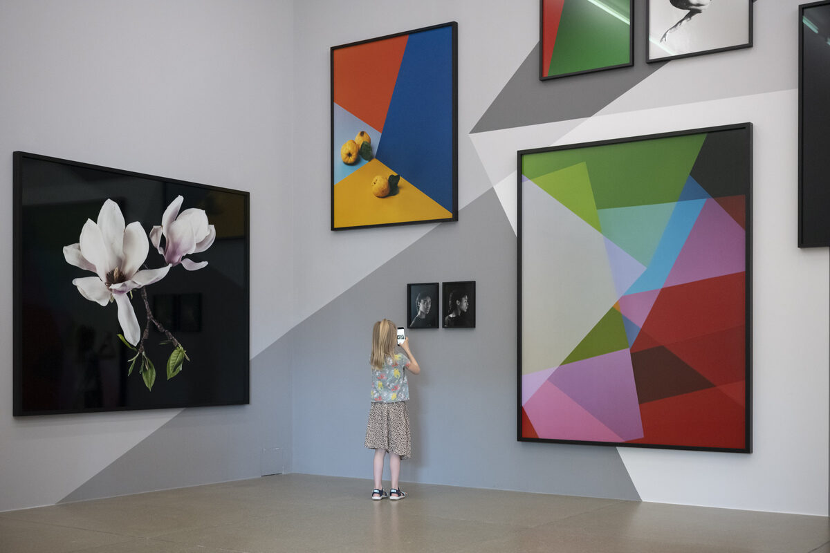 Ein Kind, das vor mehreren farbigen, abstrakten Fotografieren auf einer mit grauen Muster bemalten Wand steht