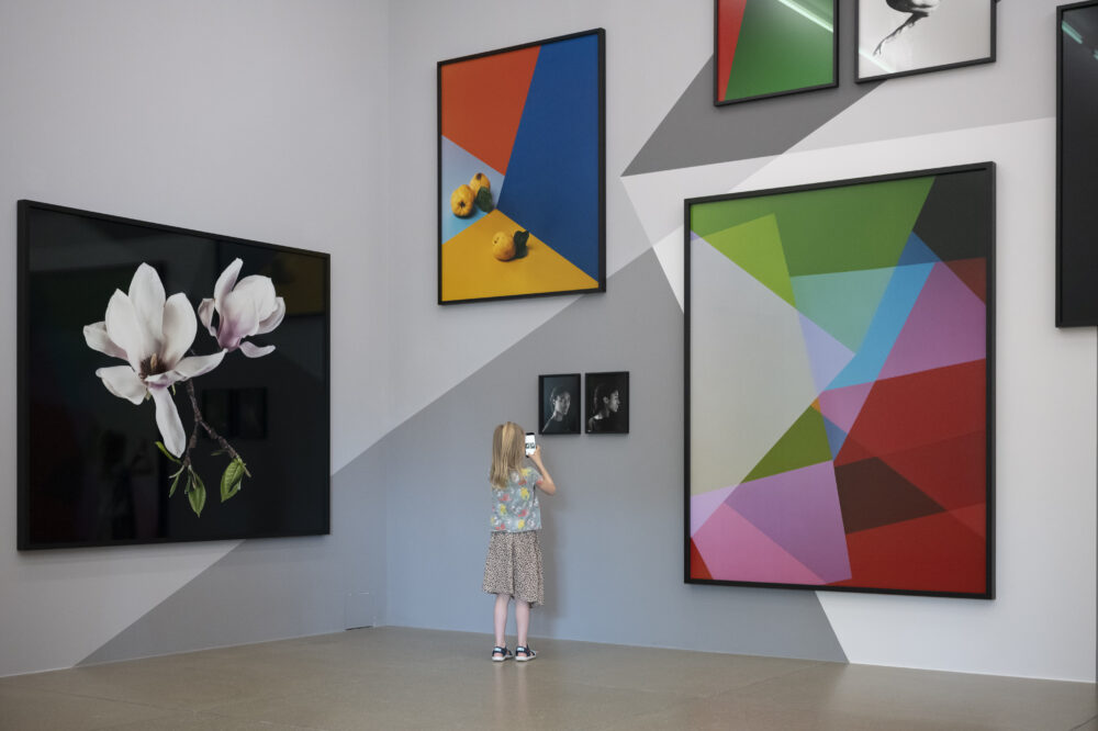 Ausstellungsansicht mit verschiedenen farbigen, abstrakten Fotografieren auf einer mit grauen Muster bemalten Wand mit einem Kind, das ganz nahe an der Wand steht, im Aargauer Kunsthaus