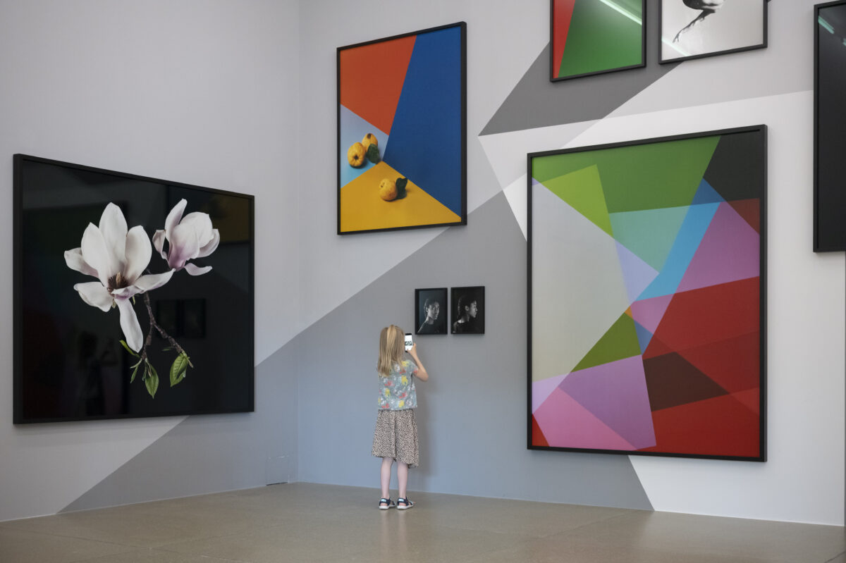 Ausstellungsansicht mit verschiedenen farbigen, abstrakten Fotografieren auf einer mit grauen Muster bemalten Wand mit einem Kind, das ganz nahe an der Wand steht, im Aargauer Kunsthaus