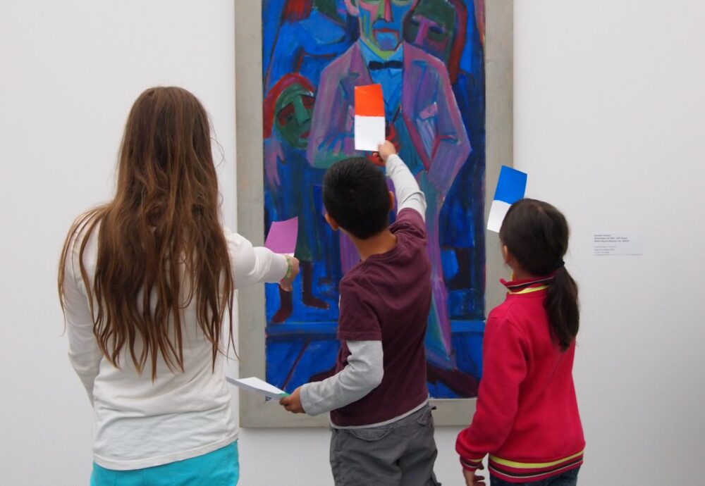 Kinder vergleichen Farben auf Farbkarten vor einem Gemälde