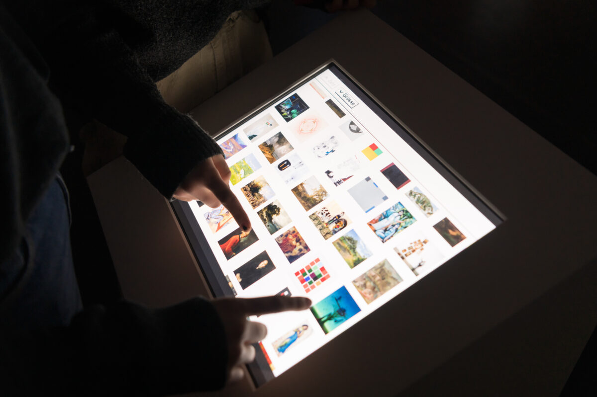 Personen wählen BIlder auf einem Bildschirm aus, die auf eine Wand neben ihnen projetziert werden.