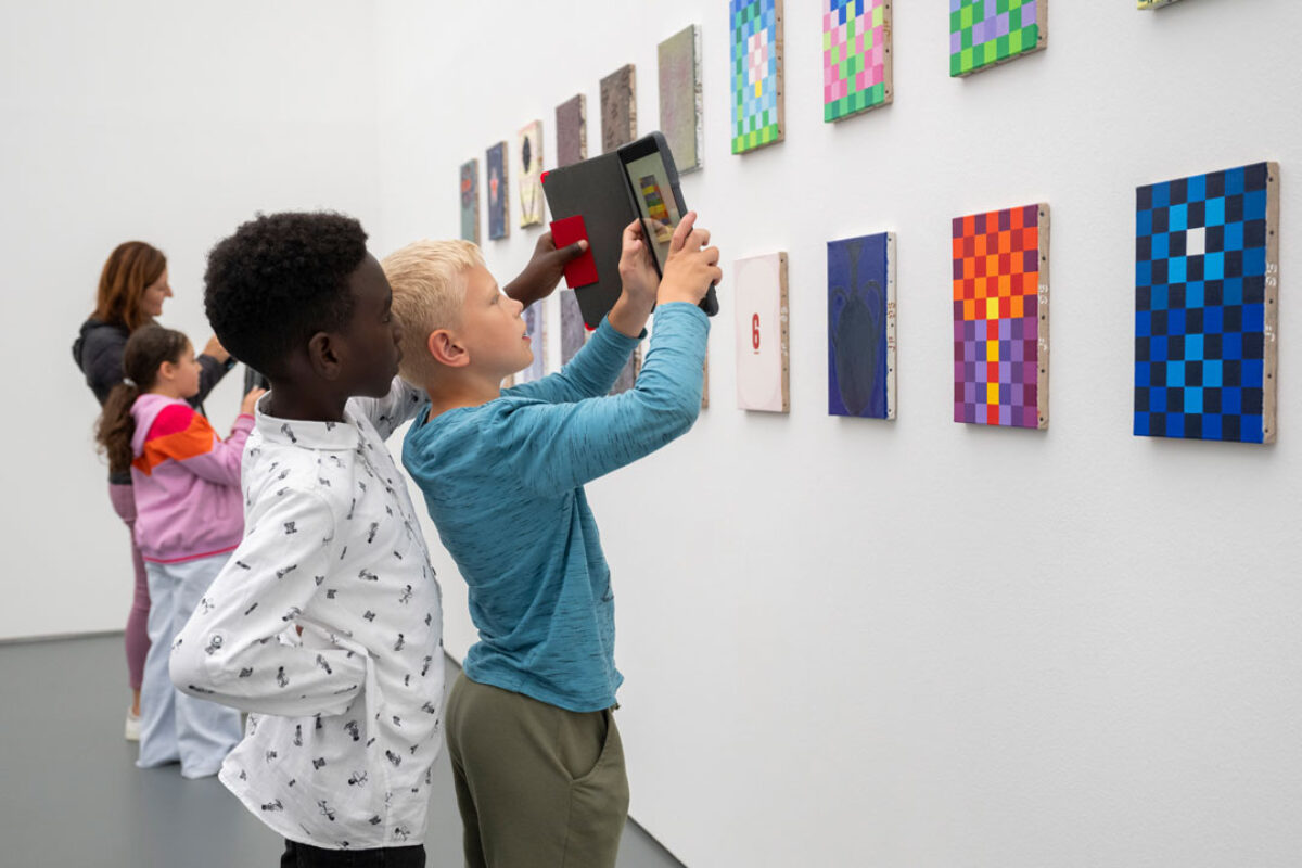 Kinder schauen mit einem Tablet in der Hand auf ein Sammlungswerk und erleben dank Augmented Reality eine animierte Version des Kunstwerkes