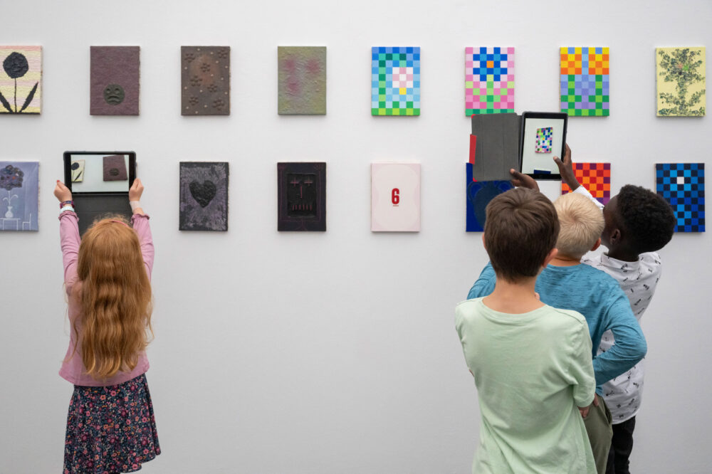 Kinder schauen mit einem Tablet in der Hand auf ein Sammlungswerk und erleben dank Augmented Reality eine animierte Version des Kunstwerkes