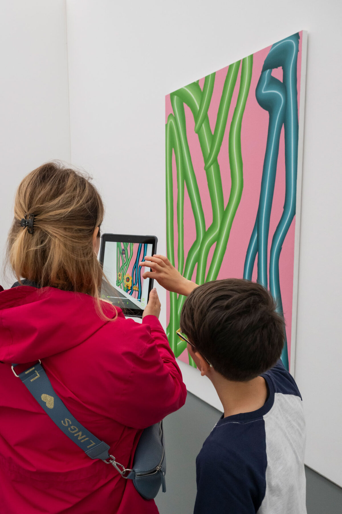 Eine Frau betrachtet mit einem Tablet ein Kunstwerk, ein Kind schaut ihr über die Schulter