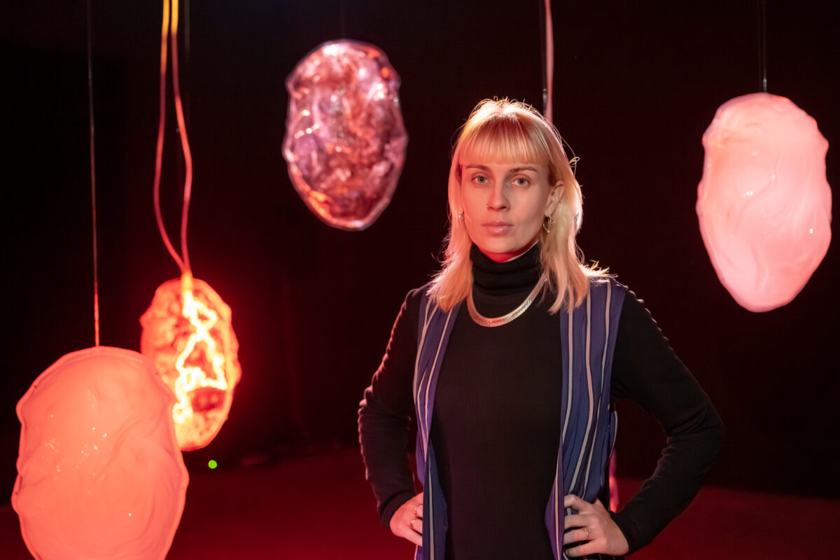 Die Künstlerin Victoria Holdt steht vor ihrer Kunstinstallation mit schwebenden Kokons.