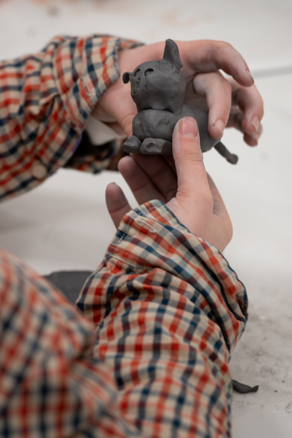 Zwei Kinderhände formen aus Ton eine Katzenfigur.