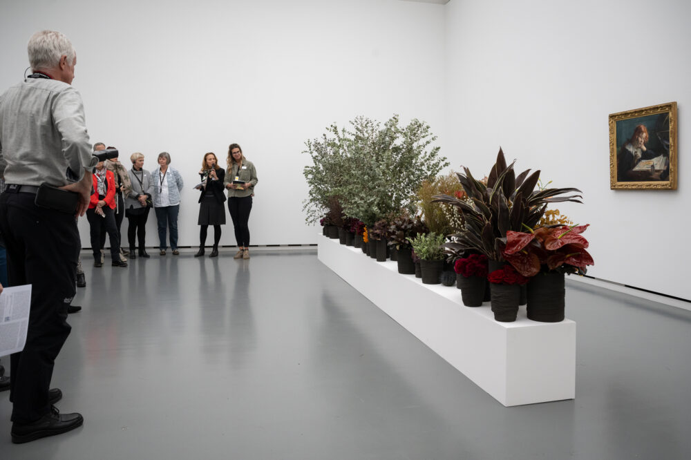 Foto von Personen, die vor einer Blumen für die Kunst Installation stehen