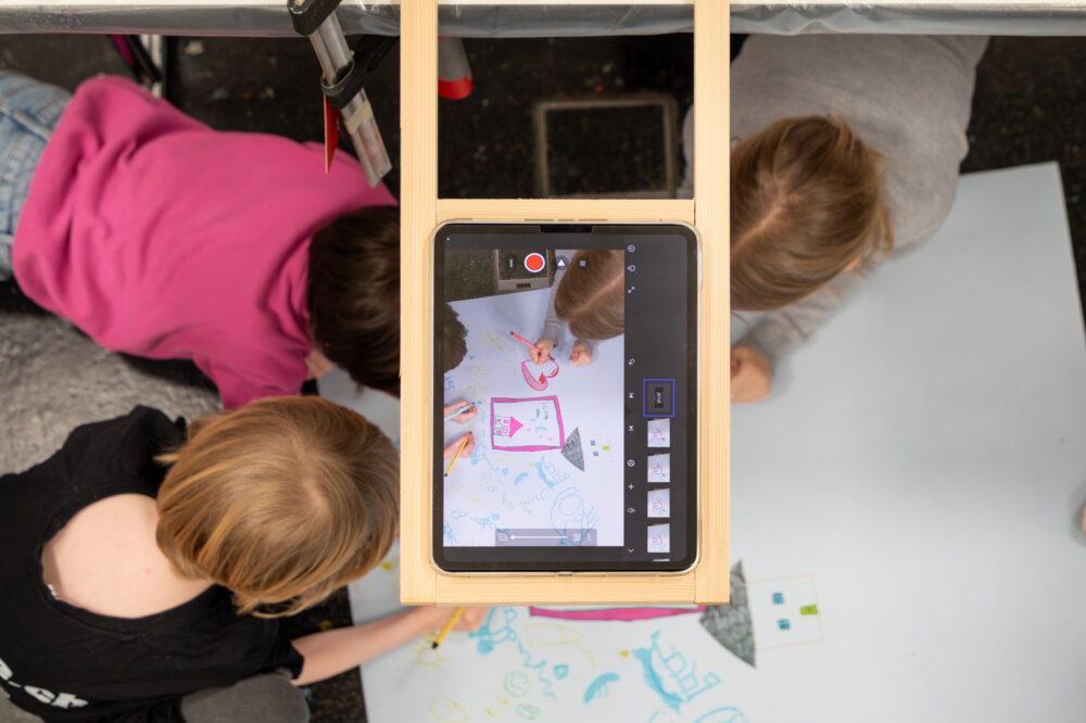 Kinder zeichnen unter einem iPad eine Folie für einen Trickfilm.