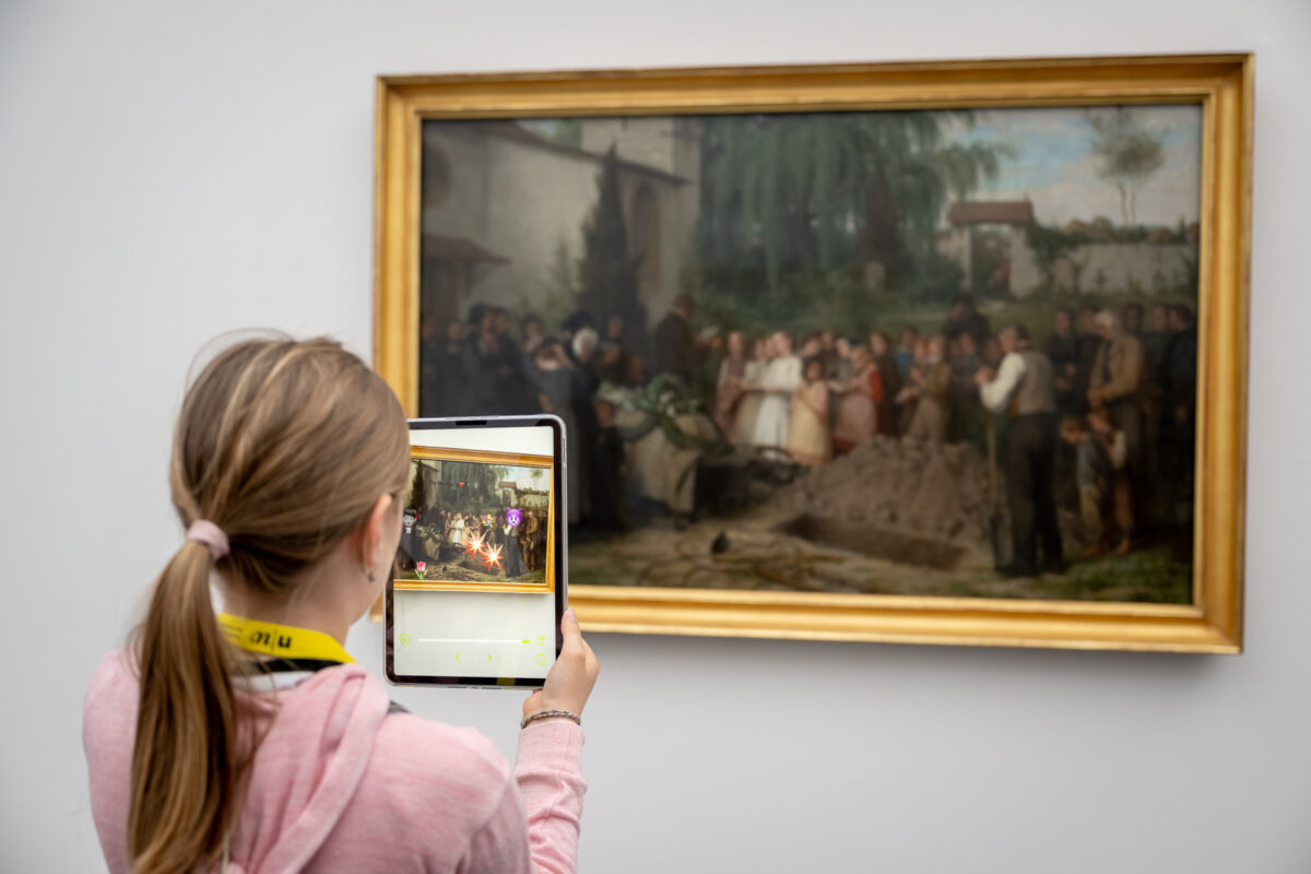 Kinder schauen mit einem Tablet in der Hand auf ein Sammlungswerk und erleben dank Augmented Reality eine animierte Version des Kunstwerkes