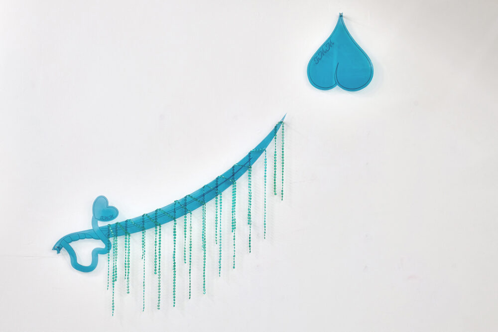 Foto eines Werks von Shamiran Istifan, das an einer Wand einen Säbel zeigt, der auf ein umgekehrtes Herzsymbol gerichtet ist.