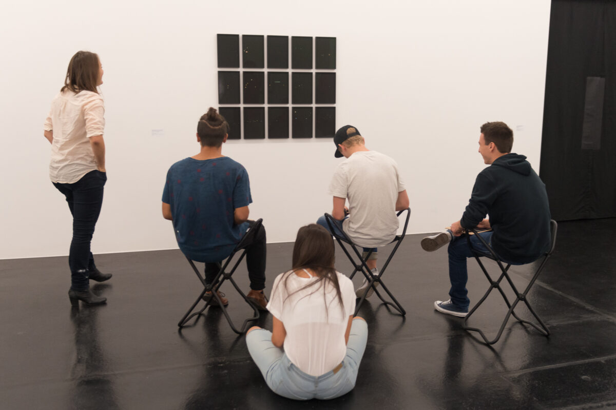 Eine Vermittlungsperson erklärt Jugendlichen ein Kunstwerk