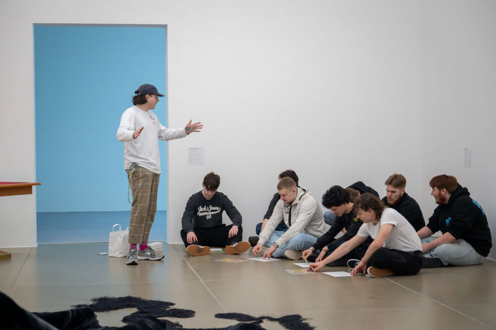 Eine Vermittlungsperson erklärt Jugendlichen ein Kunstwerk