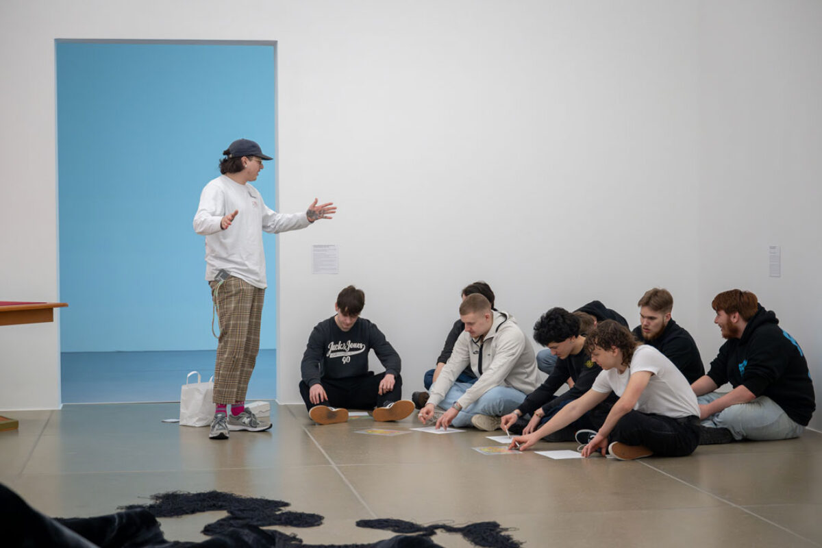 Eine Vermittlungsperson erklärt Jugendlichen ein Kunstwerk