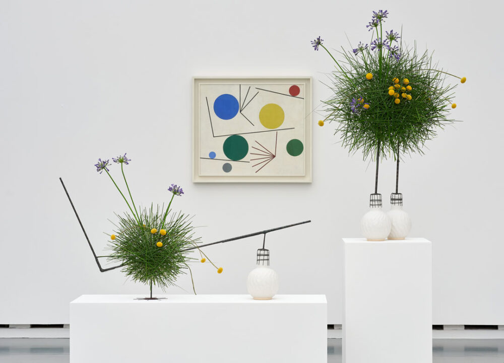 Floral gebildete Kugeln aus Gras stehen vor einem abstrakten Kunstwerk
