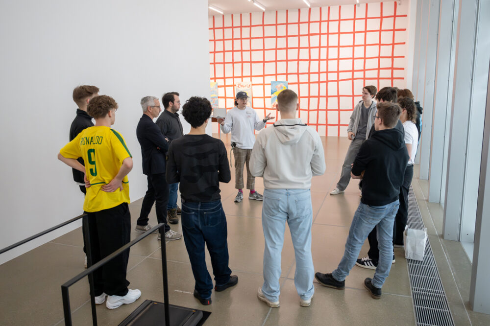 Eine Vermittlungsperson erklärt einer Schulklasse ein Werk.