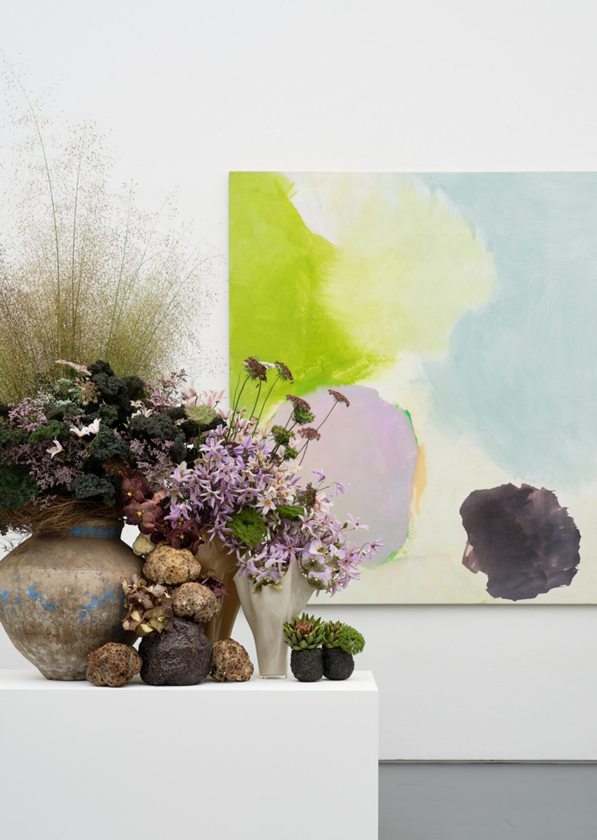 Eine Blumen-Installation mit verschiedenen Vasen steht vor einem abstrakten Kunstwerk mit Farbflächen.