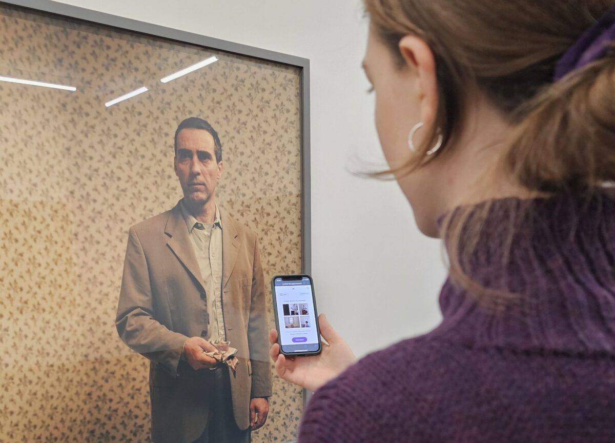 Eine Person spielt ein digitales Spiel auf dem Smartphone vor einem Kunstwerk von Teresa Hubbard / Alexander Birchler.