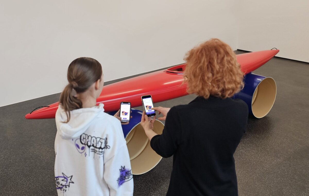 Zwei Personen spielen ein digitales Spiel auf dem Smartphone vor einem Kunstwerk von Roman Signer.
