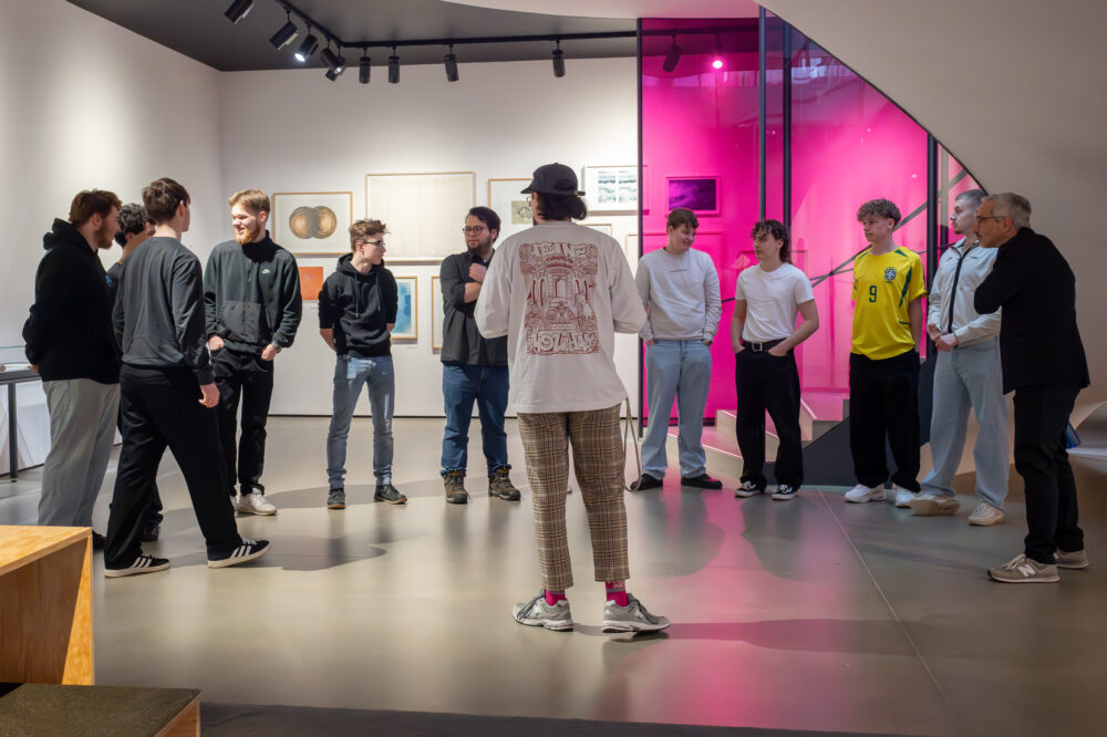 Eine Schulklasse hört einem Vermittler zu im Freiraum des Kunsthauses.