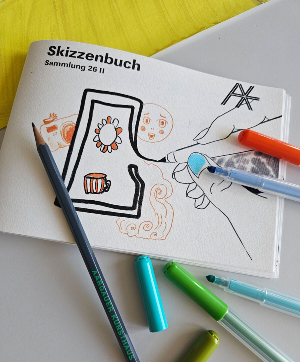 Foto des Skizzenhefts mit Stiften, die darüber gelegt sind.