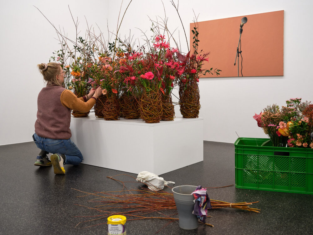 Eine Floristin stellt ein florales Werk vor einem Bild von Guido Nussbaum zusammen.