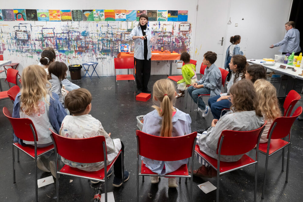 Eine Vermittlerin erklärt Kindern eine Aufgabe im Atelier.