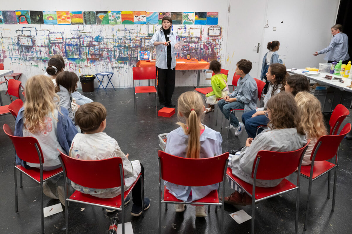 Eine Vermittlerin erklärt Kindern eine Aufgabe im Atelier.
